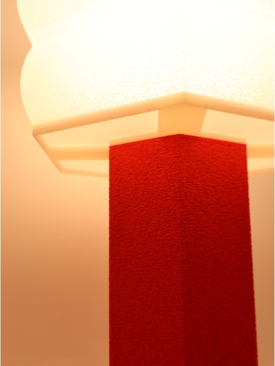 Lampe design Jacqueline allumée, lumière chaude et douce, contraste pied rouge et abat-jour crème, ambiance cosy.