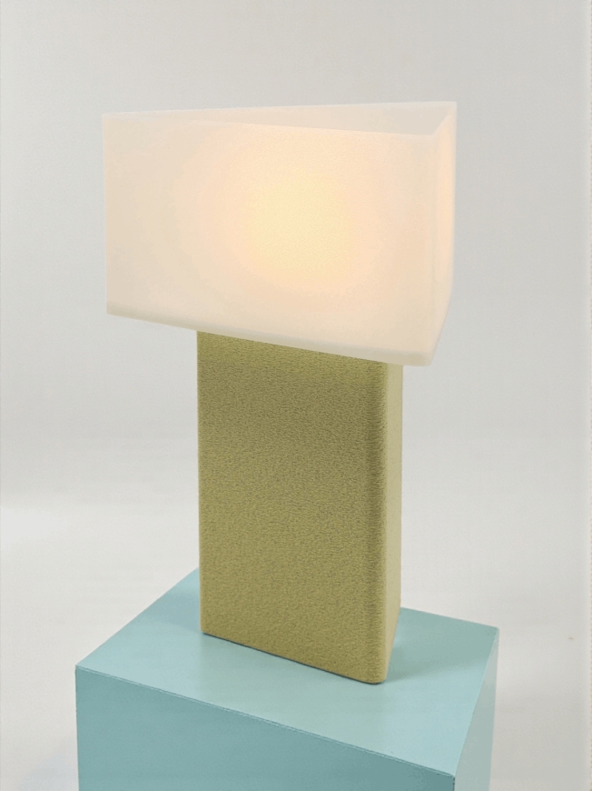 Lampe à poser design Maelle granit vanille allumée sur socle bleu, lumière douce, ambiance minimaliste.