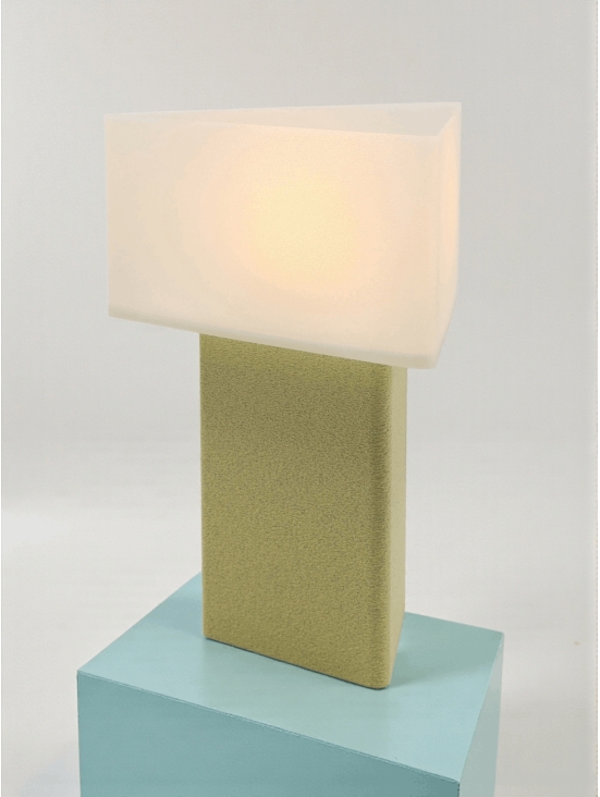 Lampe à poser design Maelle granit vanille allumée sur socle bleu, lumière douce, ambiance minimaliste.