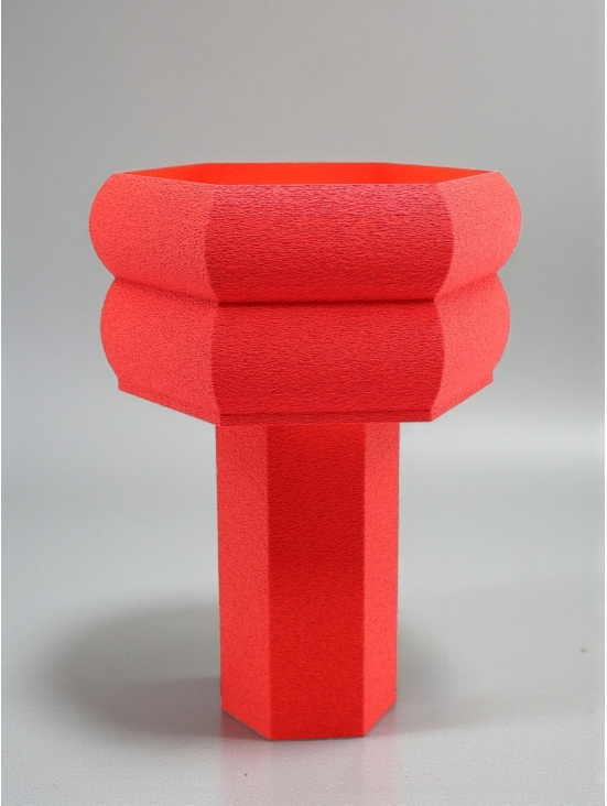 Lampe à poser design Romy granit rouge, silhouette hexagonale sculptée, ambiance studio sur fond gris doux.