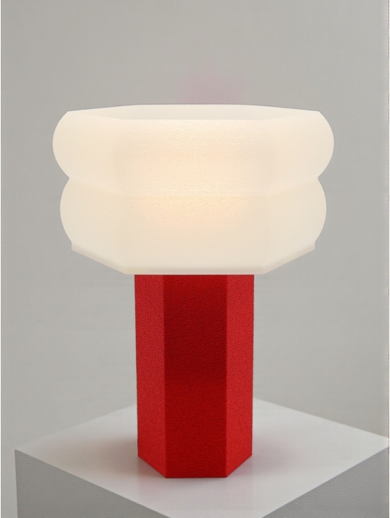 Lampe à poser design Jacqueline granit rouge allumée, abat-jour diffuseur opale, ambiance studio douce et chaleureuse.