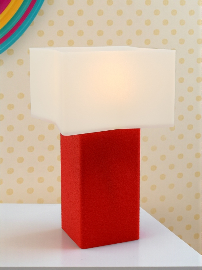 Lampe à poser Priscilla Pop Essentiel rouge allumée, abat-jour blanc lumineux, ambiance rétro avec mur à pois beige.