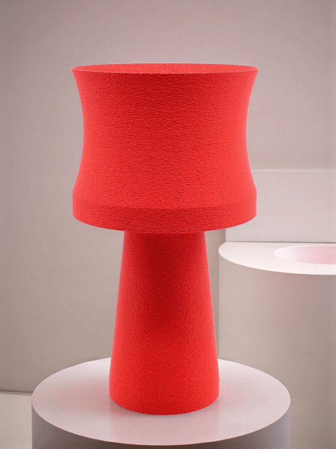 Lampe à poser design Agathe granit rouge sur socle rond blanc, ambiance douce et minimaliste, mur clair.