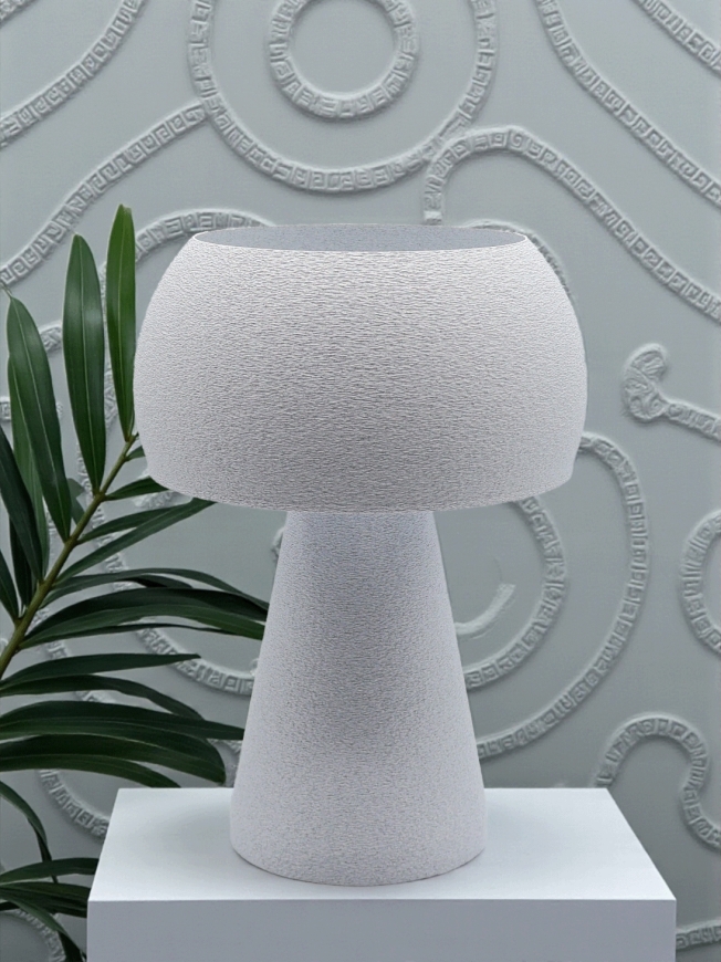 Lampe à poser design Agnès granit pierre sur socle blanc, ambiance minérale avec plante verte et mur texturé.