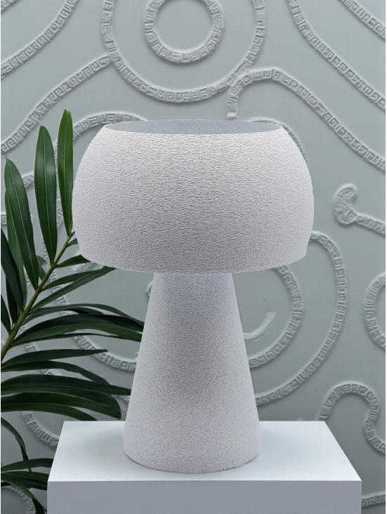 Lampe à poser design Agnès granit pierre sur socle blanc, ambiance minérale avec plante verte et mur texturé.