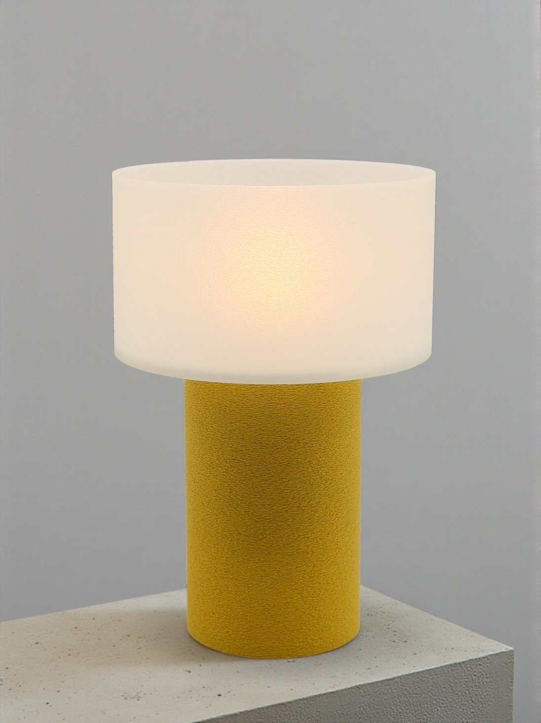 Lampe à poser design Clarisse granit jaune allumée sur socle béton, lumière douce, ambiance minimaliste.