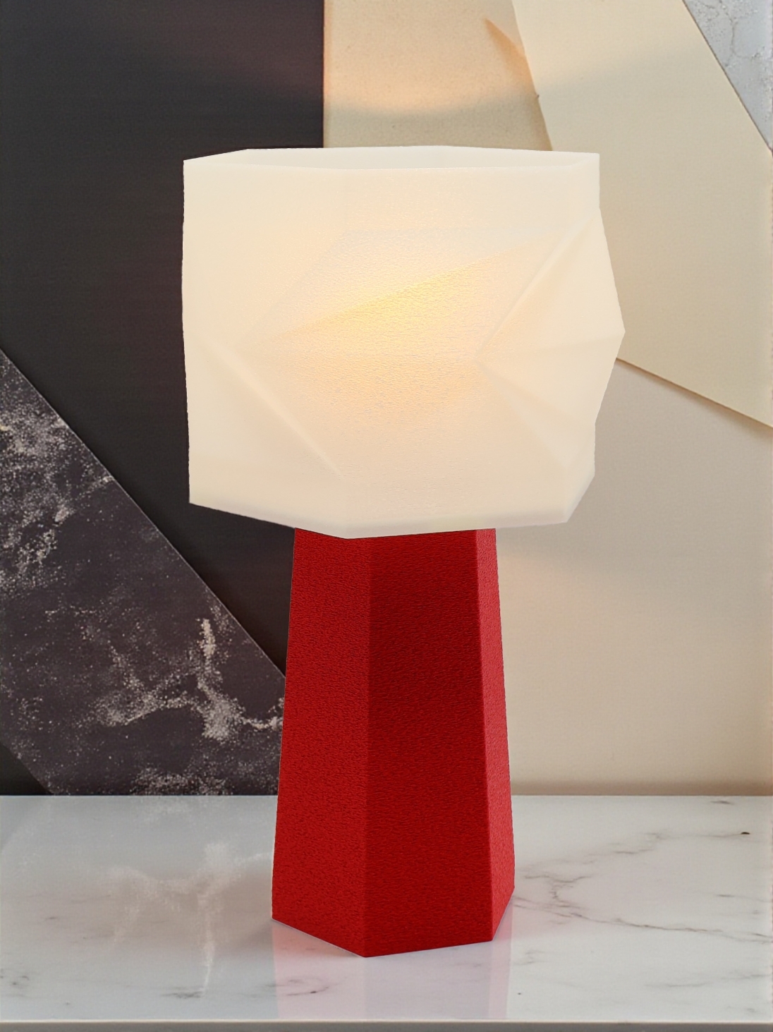Lampe à poser design Élise granit rouge allumée, abat-jour facetté, ambiance graphique sur table marbrée.