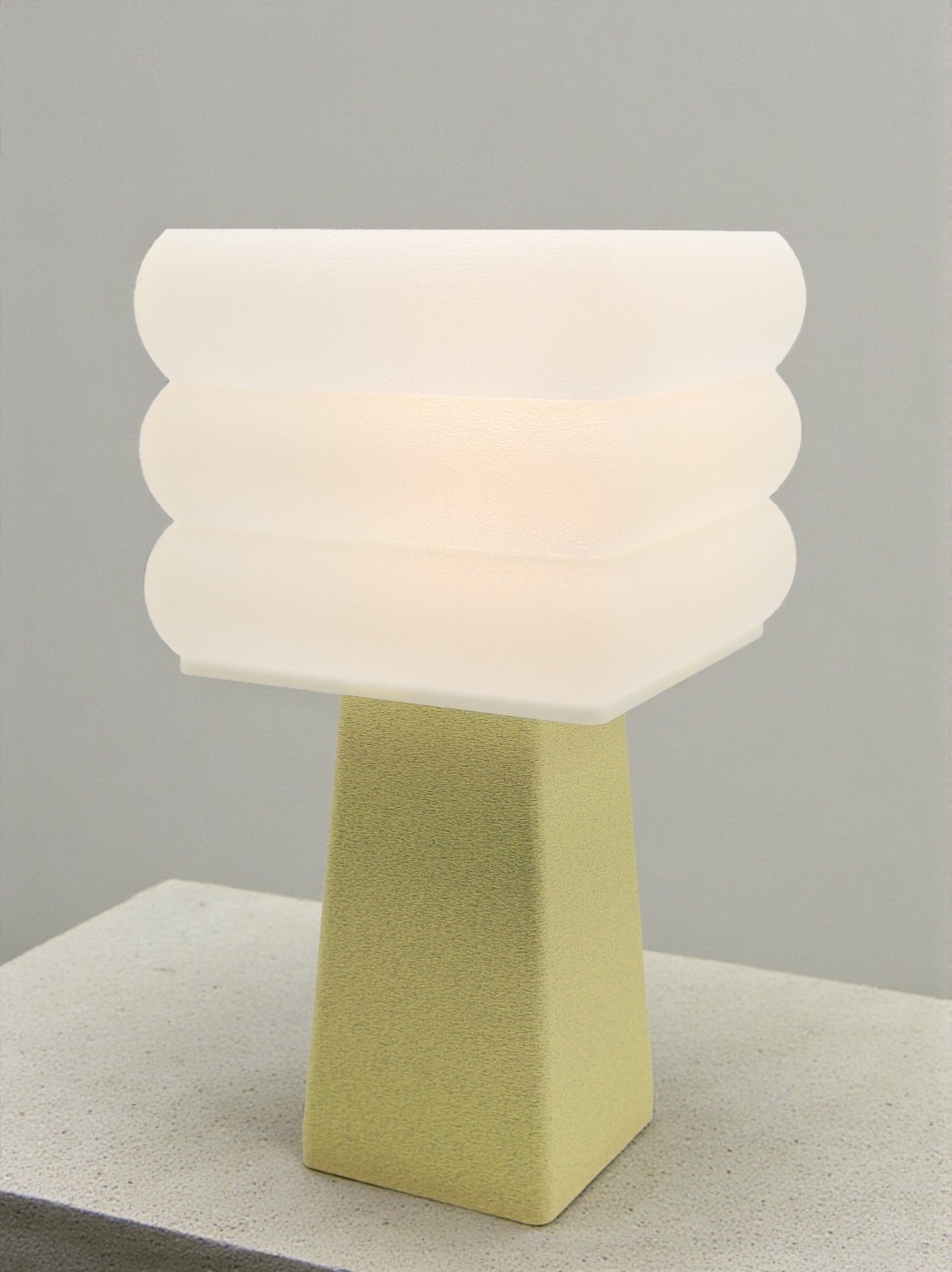 Lampe à poser design Isabelle granit vanille allumée sur socle béton, lumière douce, ambiance minimaliste.
