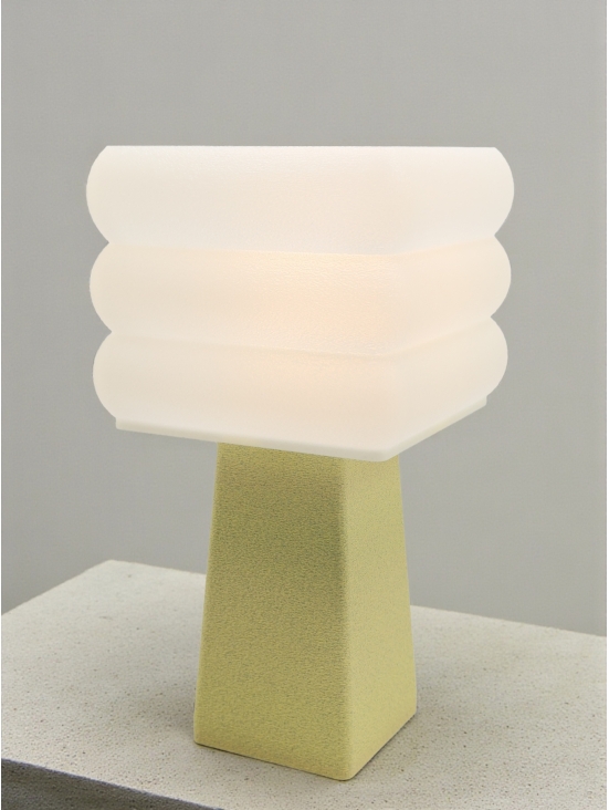 Lampe à poser design Isabelle granit vanille allumée sur socle béton, lumière douce, ambiance minimaliste.