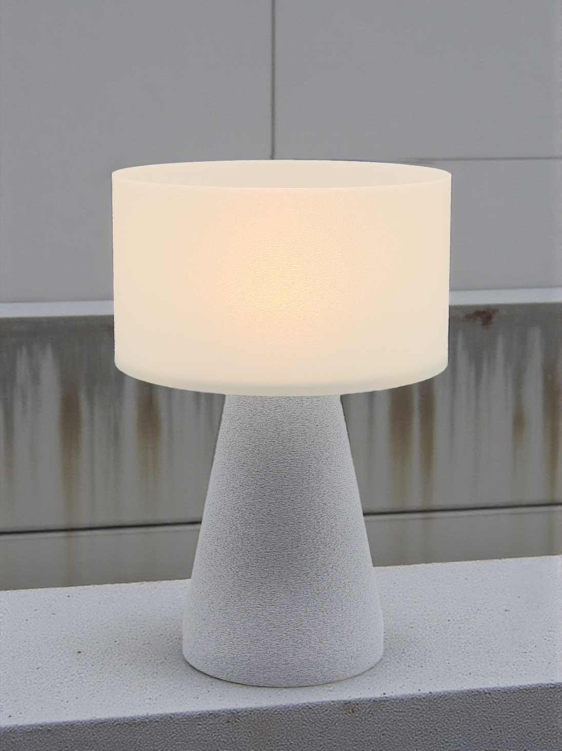 Lampe à poser design Meredith granit pierre allumée, lumière douce, ambiance industrielle sur béton et mur gris.