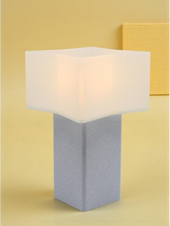 Lampe à poser design Priscilla granit pierre allumée, abat-jour géométrique, ambiance chaleureuse sur fond jaune.